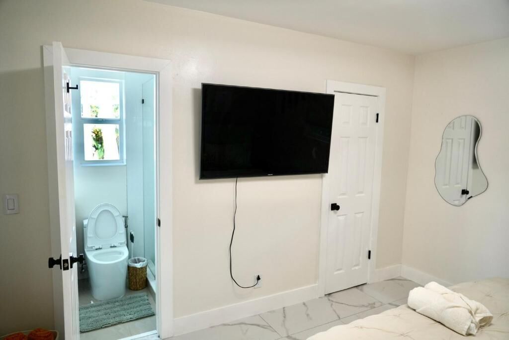 A bathroom with a toilet, a sink, a mirror, and a television mounted on the wall.