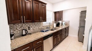 Una cocina con armarios de madera oscura, encimeras de granito, lavavajillas y refrigerador.