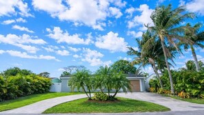 Una casa residencial con camino de entrada, palmeras y cielo despejado.