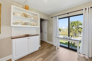 A kitchen with white cabinets, a wooden countertop, and a view of a palm tree through a large window. - Welcome to Villa E-6! (St. George Island)