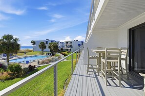 A balcony with a pool, chairs, and a view of the ocean and buildings. - Welcome to Villa E-6! (St. George Island)