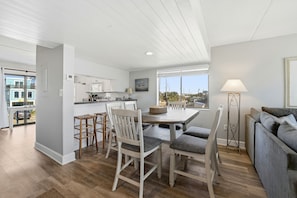A modern kitchen with white cabinets, a dining table with chairs, and a view through large windows. - Welcome to Villa E-6! (St. George Island)