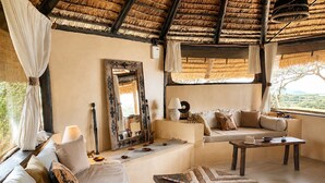 A room with a thatched roof, a sofa, a table with books, and a mirror. - Nasuulu lodge (Isiolo)