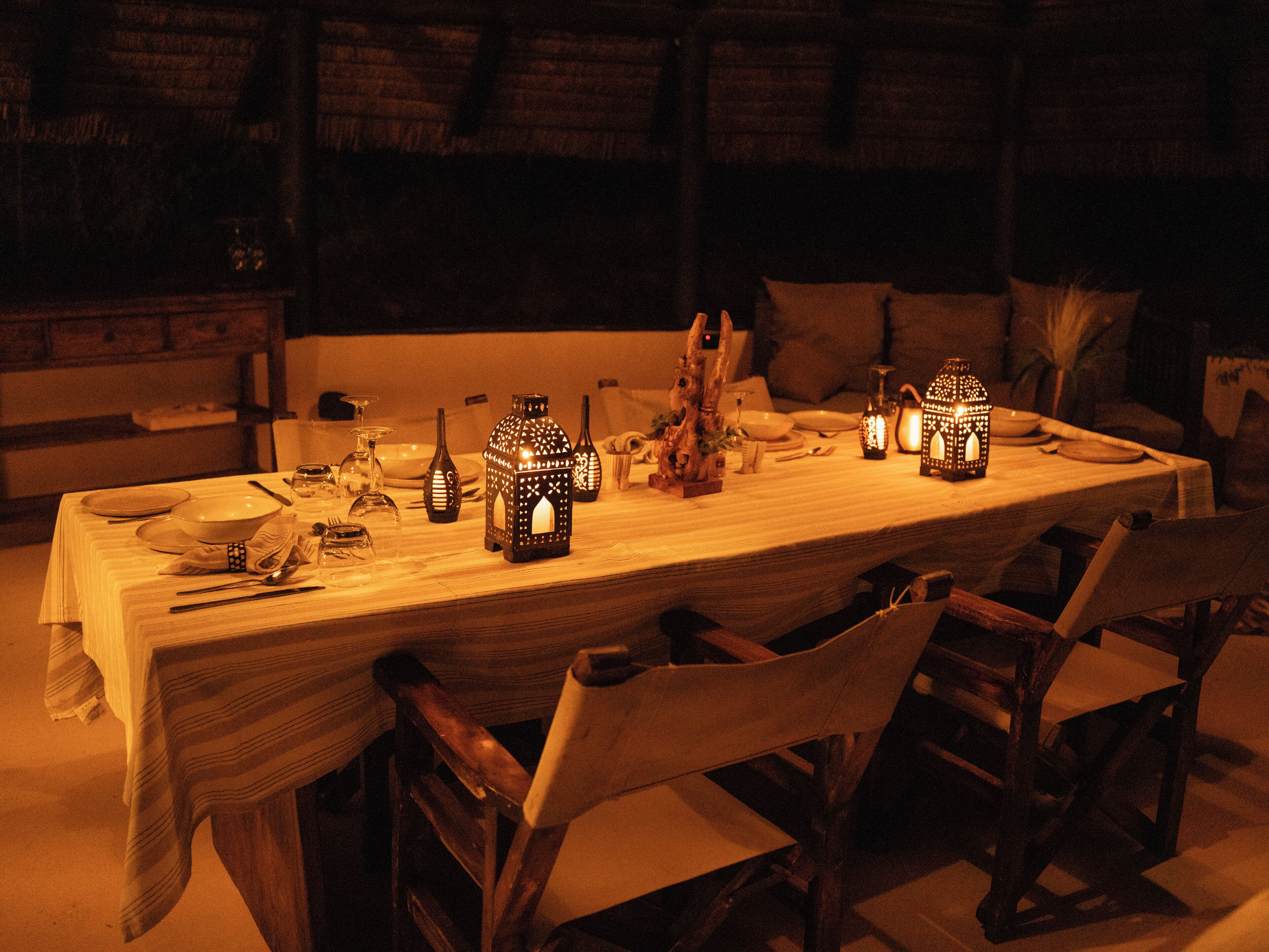 Una mesa de comedor dispuesta con velas, platos y cubiertos, rodeada de sillas.