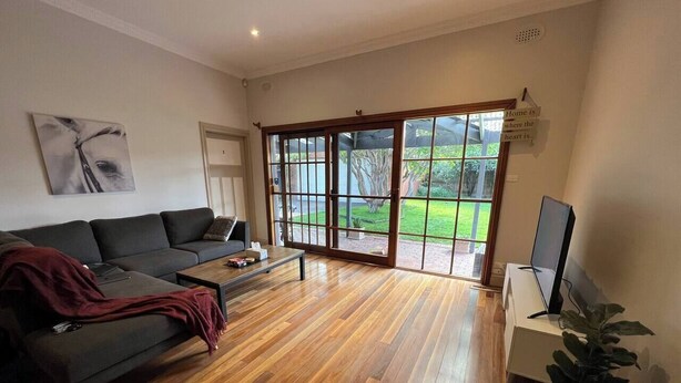 A modern living room with a dark sofa, a coffee table, a TV, and a large sliding glass door leading to a garden.