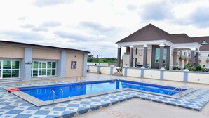 A swimming pool with a tiled deck, a building with a flat roof, and a clear sky.