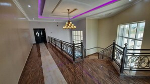 A spacious hallway with a marble floor, a chandelier, and a staircase with ornate railings.
