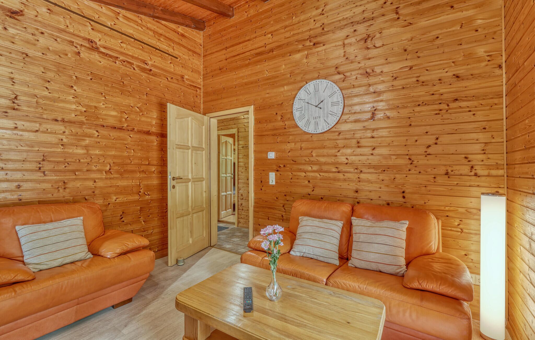 Interior de madera con dos sofás de cuero, una mesa de centro de madera, un reloj de pared y una puerta que da a otra habitación.