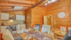 A wooden interior with a dining table set for four, a kitchen area, and a living space with a sofa and a clock on the wall.