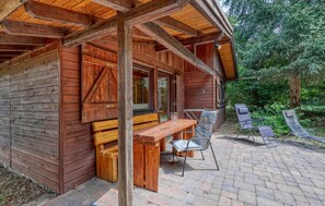 A wooden cabin with a patio area featuring a table and chairs, surrounded by trees. - Stunning home in Merzalben with sauna (Merzalben)