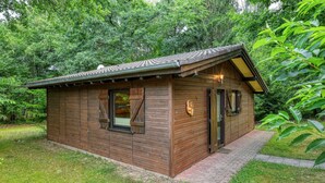 A small wooden cabin with a tiled roof, a window with shutters, and a door with a number plate.