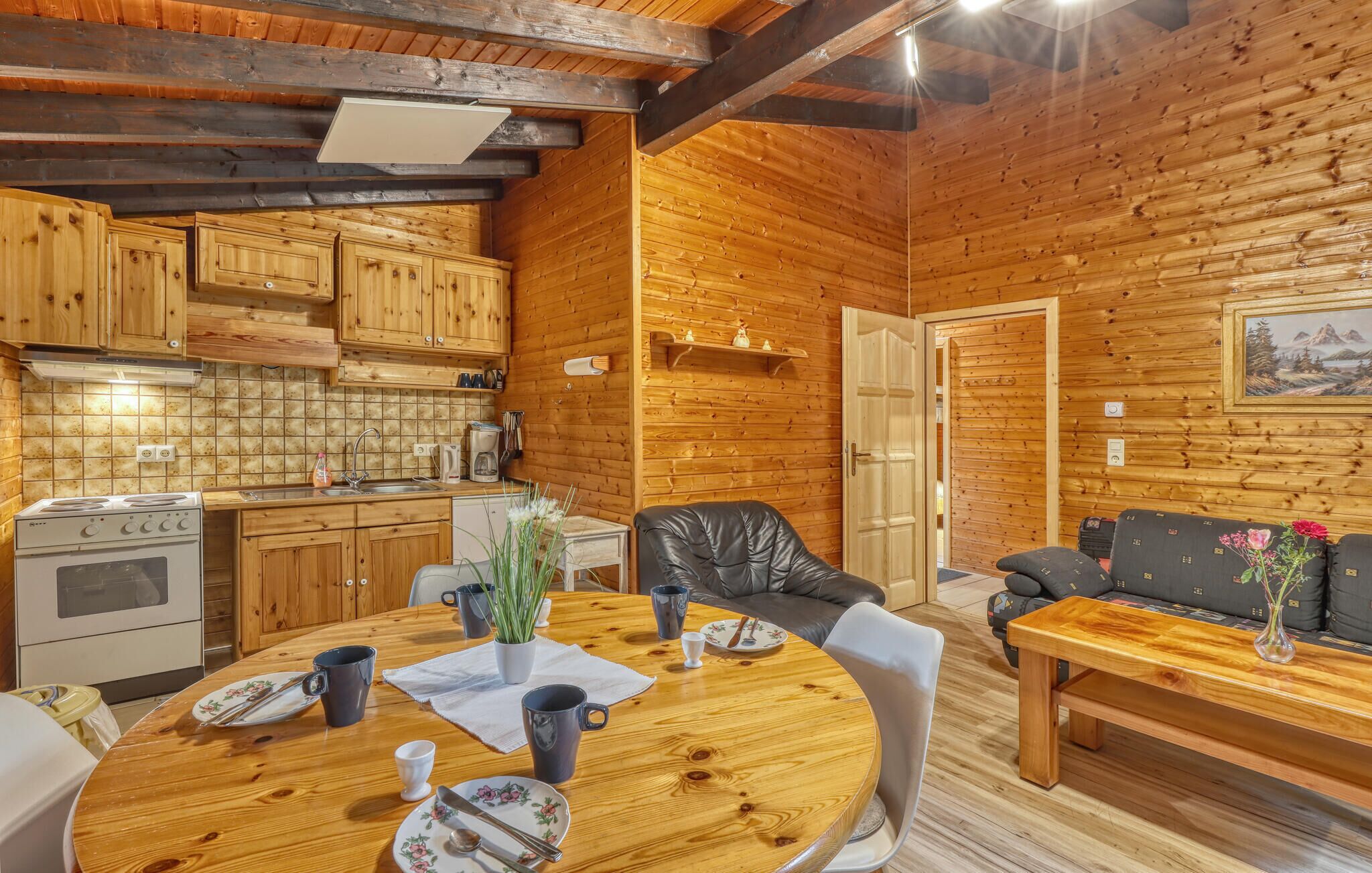 L’intérieur d’un chalet accueillant, avec un décor en bois, une table à manger mise avec des assiettes et des tasses, un canapé et un coin cuisine équipé d’une cuisinière et de placards.