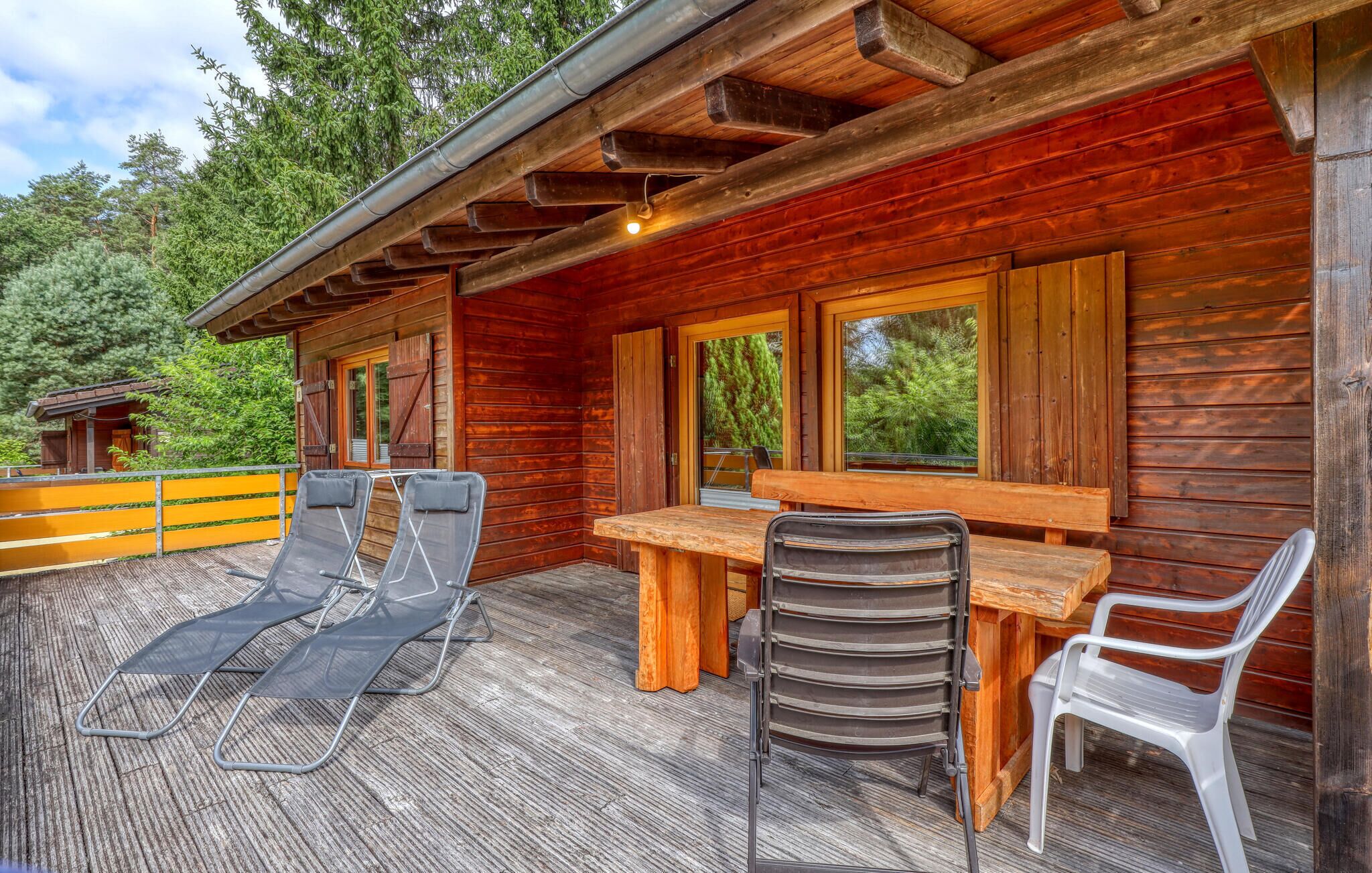 Une terrasse en bois avec une table et des chaises, un espace couvert avec un toit, et une vue sur les arbres.