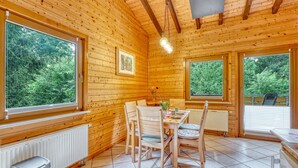 En stuga byggd av trä med ett matområde, stora fönster och utsikt över grönskan.