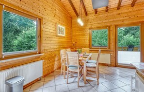 Eine Holzhütte mit Essbereich, großen Fenstern und Blick auf Grünflächen.