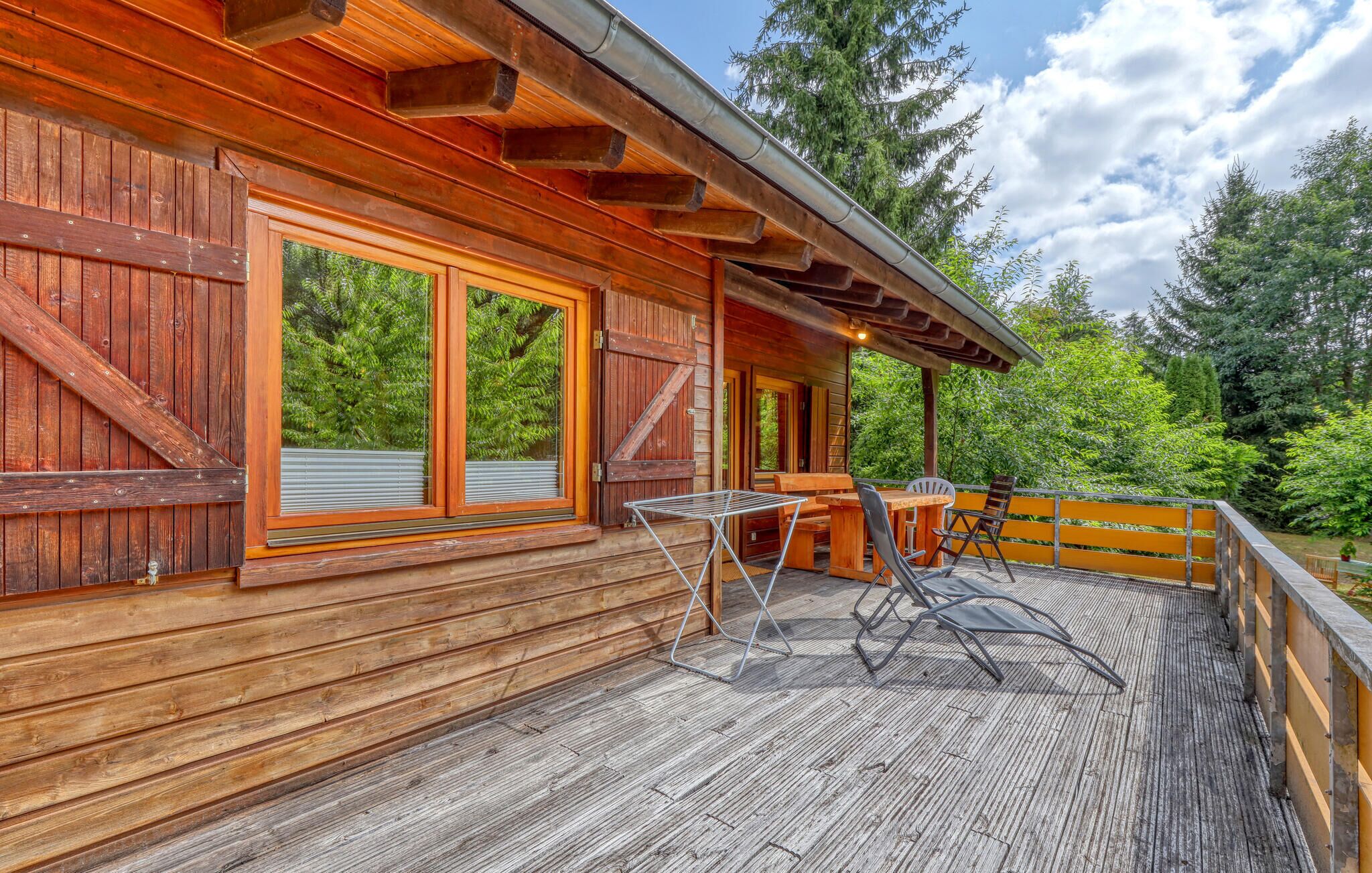 A wooden cabin with a deck, large windows, and a covered outdoor seating area.