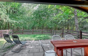 Eine Terrasse im Freien mit einem Holztisch und -stühlen, umgeben von einem Holzzaun und üppiger Bepflanzung.