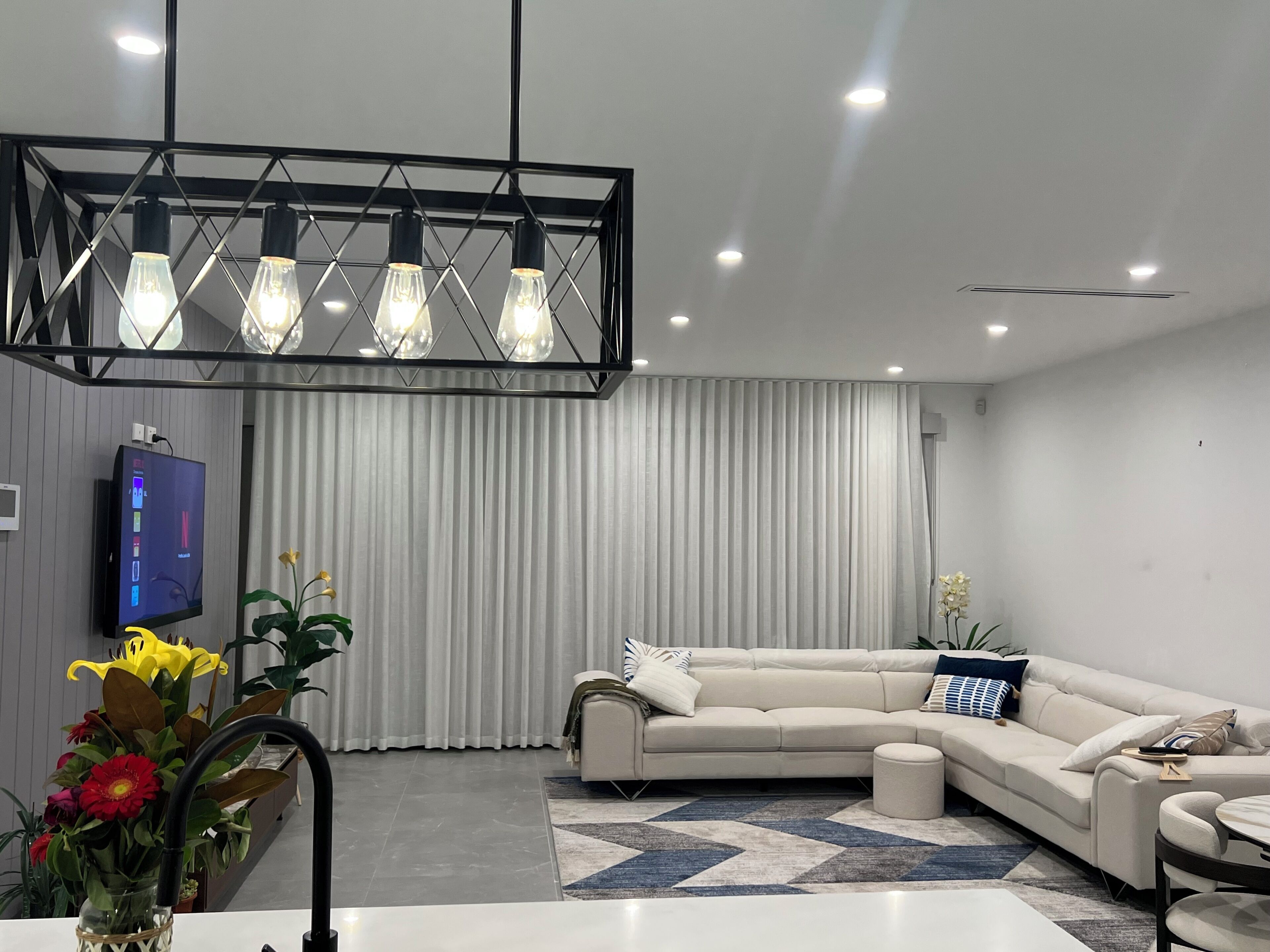 A modern living room with a sectional sofa, a TV mounted on the wall, and a decorative light fixture.
