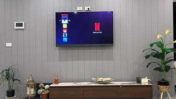 A modern living room with a flat-screen TV mounted on a grey wall, a wooden entertainment unit below, and a potted plant to the right.