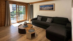 A living room with a sofa, a coffee table, and a view of a balcony with outdoor furniture. - Chamonix Town Centre Apartment with Free Parking (Chamonix-Mont-Blanc)
