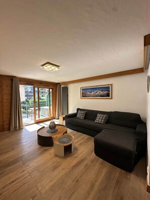 Ein Wohnzimmer mit einer Couch, einem Couchtisch und Blick auf einen Balkon mit Gartenmöbeln.