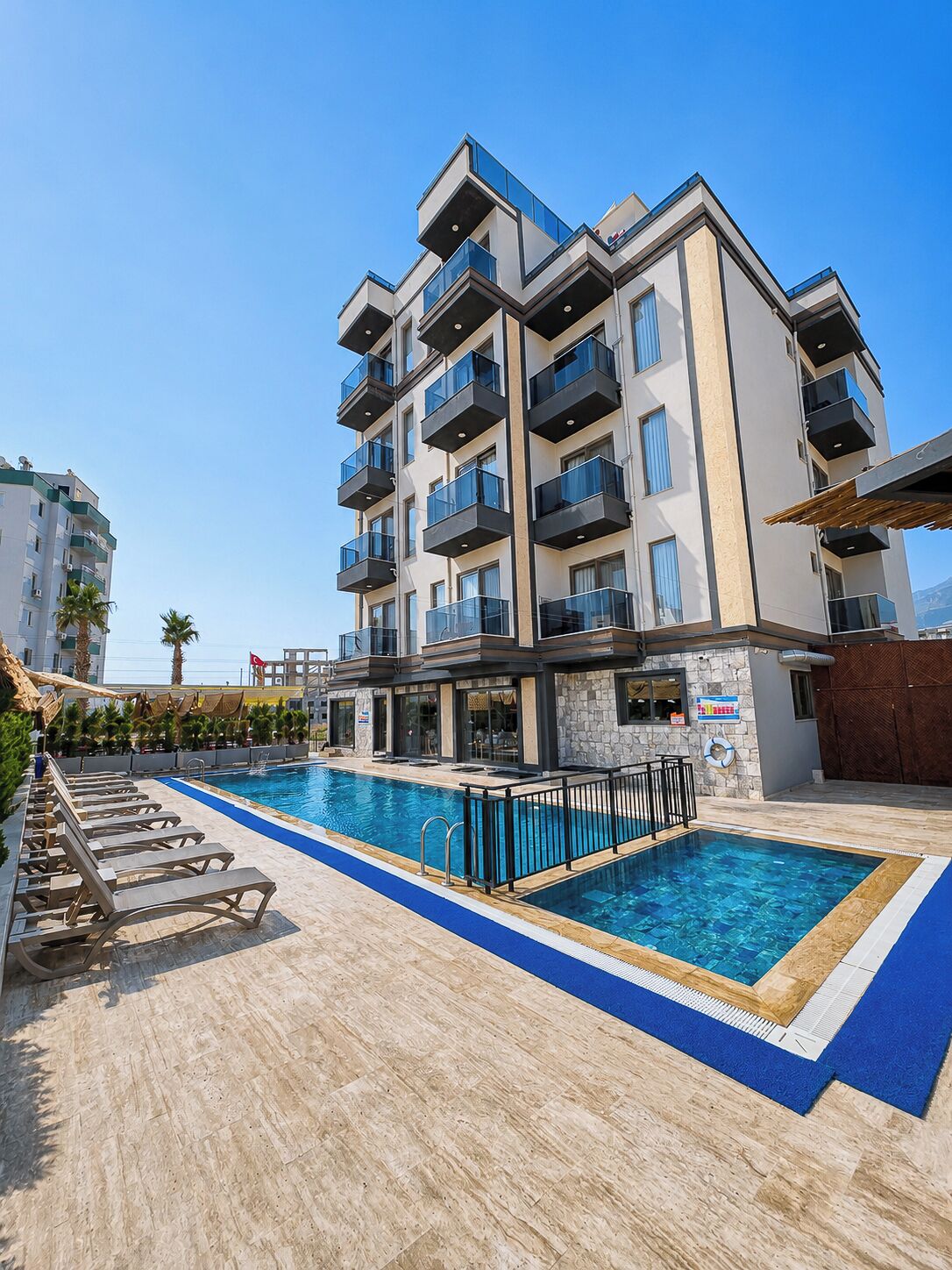 A modern hotel with a swimming pool, multiple balconies, and a stone facade.