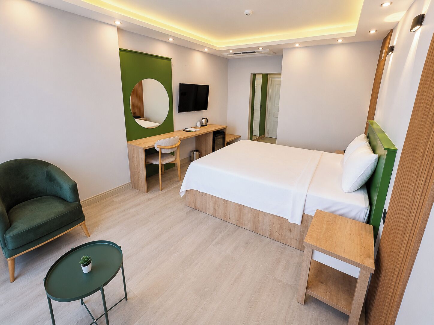 A modern hotel room with a bed, desk, chair, and a small table with a plant.