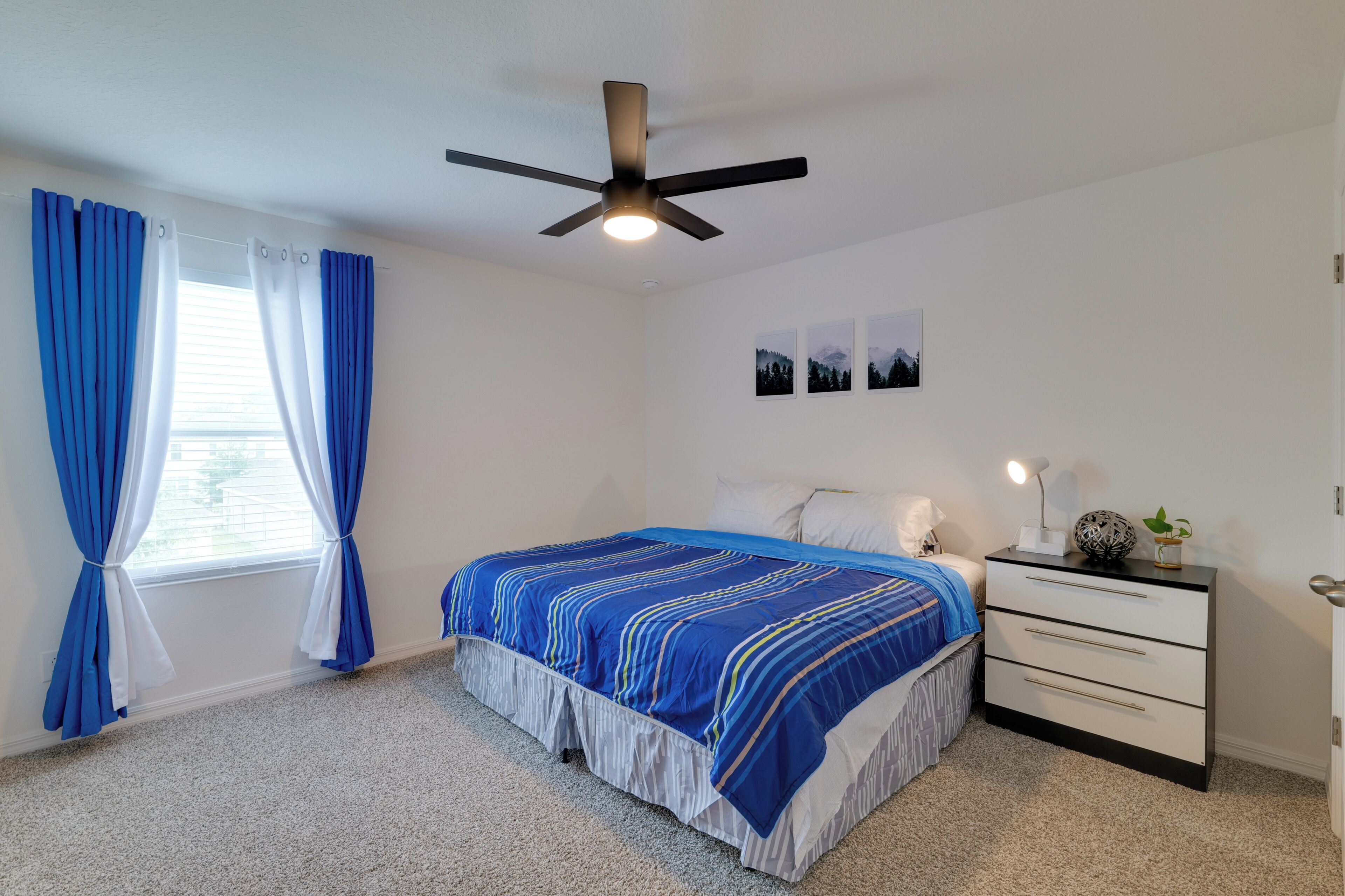 A bedroom with a bed, a ceiling fan, a nightstand, and a window with curtains.