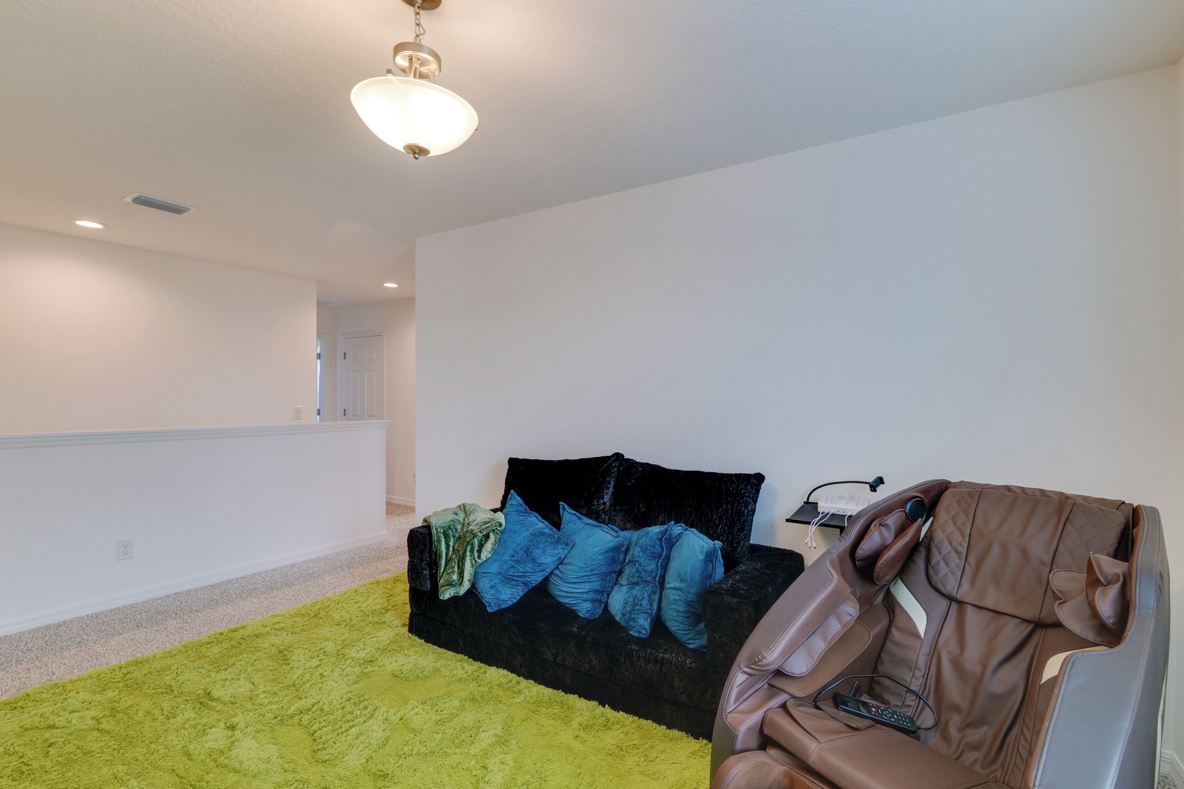 Una habitación con un sofá negro, una alfombra verde y una silla de masaje.