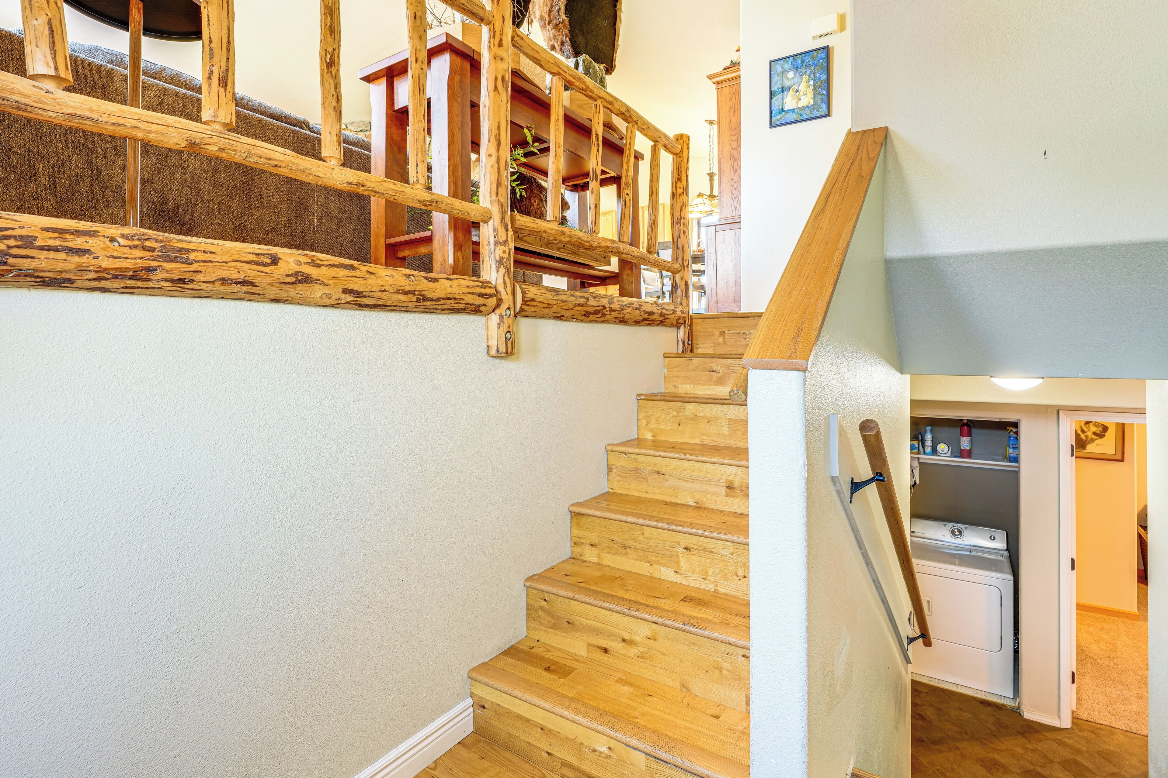 Eine Holzt Treppe mit Handlauf, die zu einem Raum mit Waschmaschine und Schrank führt.