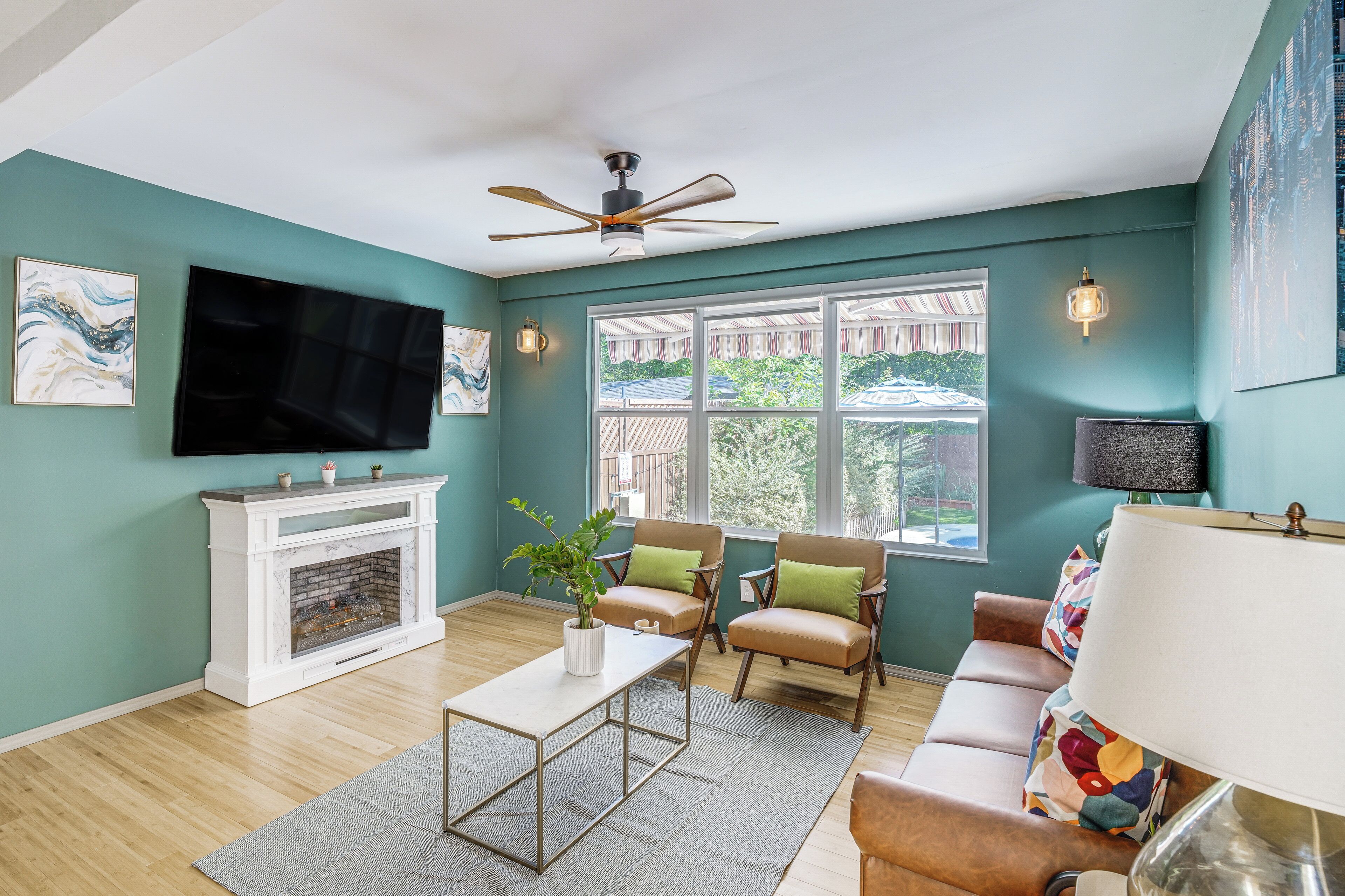 Una sala de estar con chimenea, dos sillones, un sofá, un televisor y un ventilador de techo.
