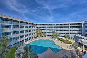 Un hotel con una piscina grande en el centro, varios balcones y un cielo azul despejado.