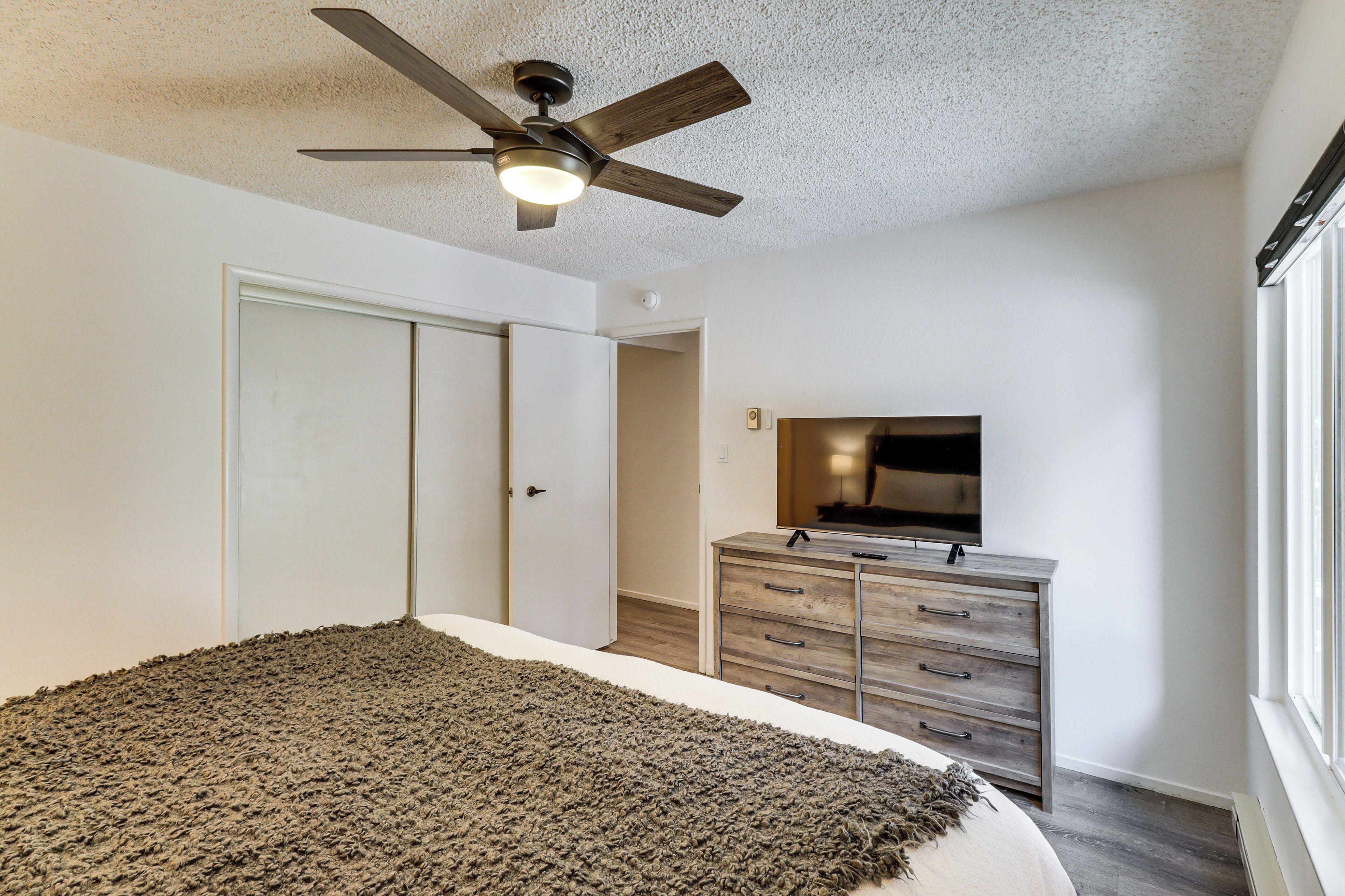 A bedroom with a bed, a ceiling fan, a dresser, and a TV.