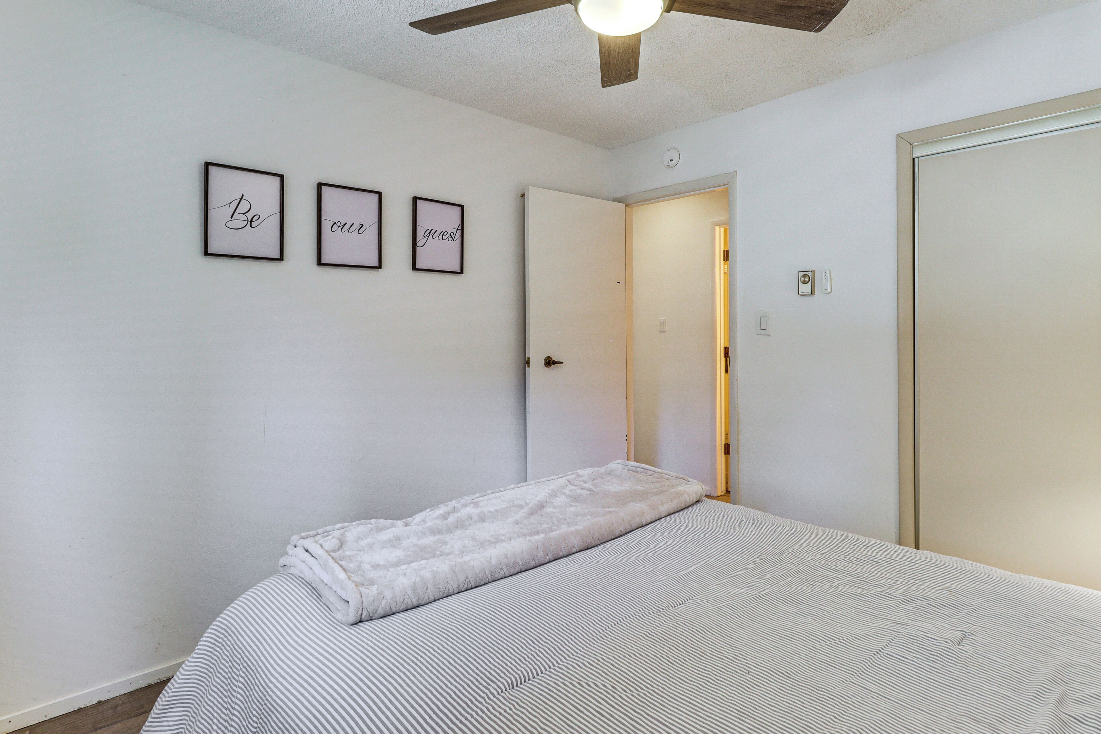 A bedroom with a bed, a ceiling fan, and a door leading to another room.