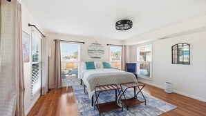 A bedroom with a bed, a bench, a window, a wall clock, and a ceiling light fixture. - Walk to Beach at the End of the Street! (St. Augustine)