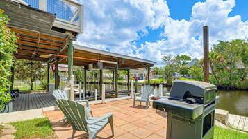 An outdoor patio with a grill, chairs, and a view of a lake.