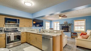 A kitchen with a stove, oven, and dishwasher, a dining area with a table and chairs, and a living room with a sofa and fireplace. - Scallop HQ: 3 Boat Docks and Free Golf Cart! (Homosassa)