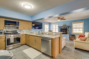 Une cuisine équipée d’une cuisinière, d’un four et d’un lave-vaisselle, un coin repas avec une table et des chaises, et un salon avec un canapé et une cheminée.