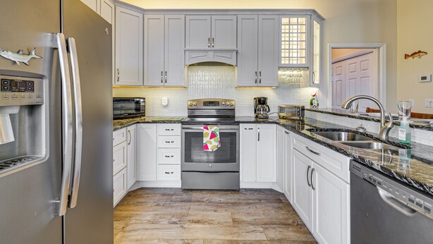 A kitchen with white cabinets, stainless steel appliances, a granite countertop, and a tiled backsplash. - Scallop HQ: 3 Boat Docks and Free Golf Cart! (Homosassa)