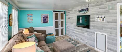 Un salon comprenant un canapé, un pouf, une lampe et un téléviseur fixé au mur.