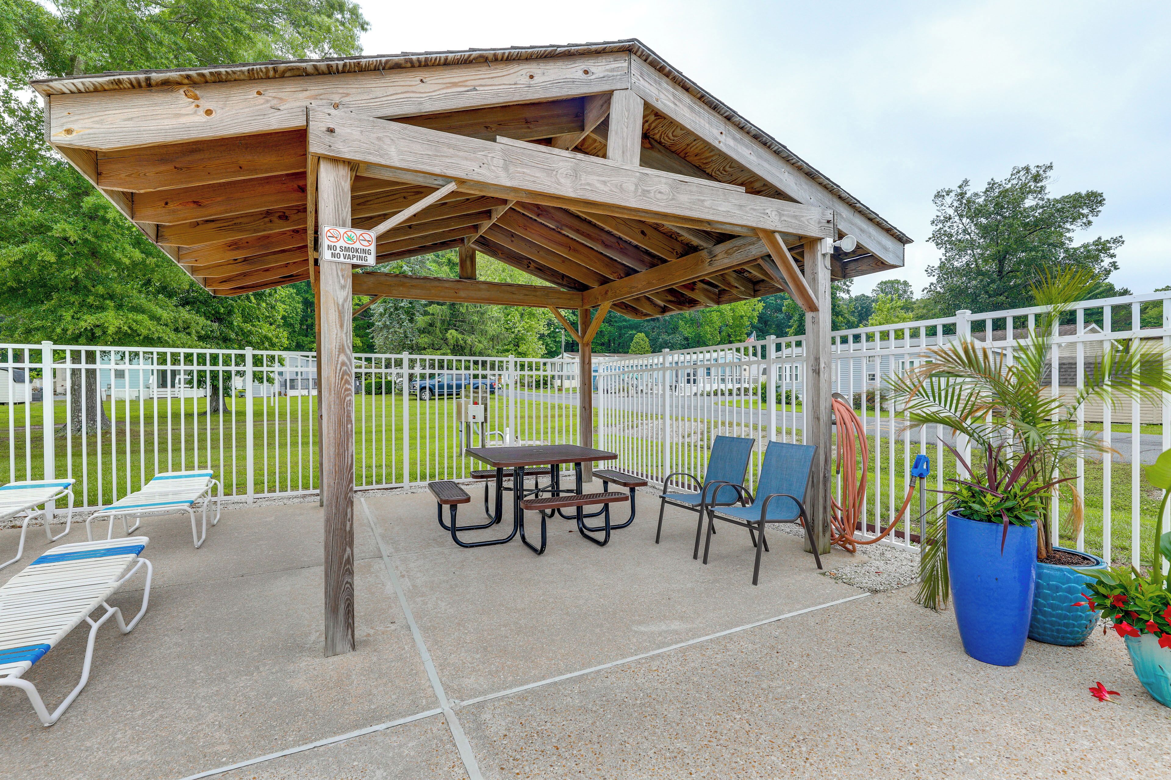 A wooden pavilion with picnic tables and chairs, surrounded by a white fence.