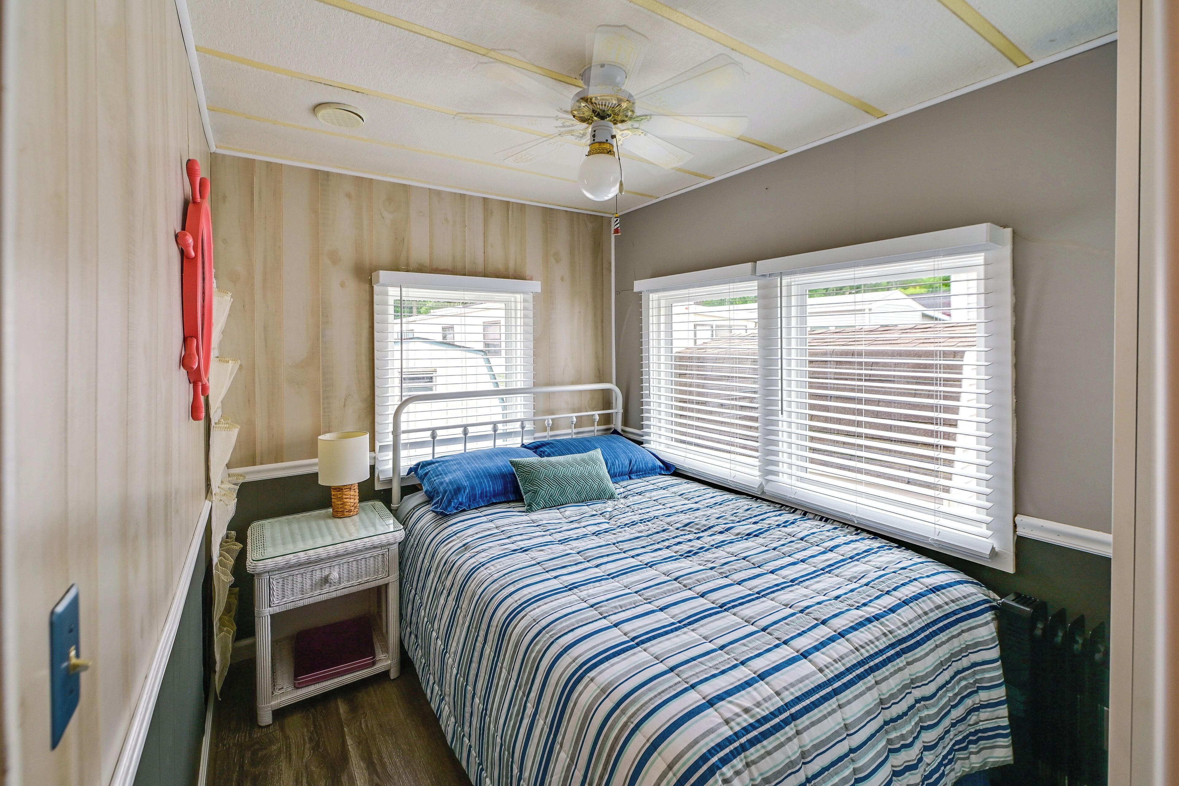A bedroom with a bed, nightstand, lamp, and two windows with blinds.