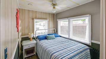 A bedroom with a bed, nightstand, lamp, and two windows with blinds.