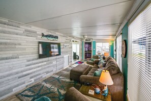 A living room with a sofa, ottoman, and a lamp. There is a television mounted on the wall and a window with blinds. - Pool + Bay Access! Home 13 Mi to Ocean City Beach (Berlin)