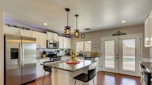 A kitchen with a central island, stainless steel appliances, and a view through the glass doors. - Pool, Games, Fenced Yard! Extended Stay in Buckeye (Buckeye)