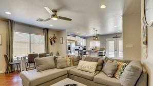 A modern living room with a sectional sofa, a dining area with chairs, a kitchen in the background, and a ceiling fan. - Pool, Games, Fenced Yard! Extended Stay in Buckeye (Buckeye)