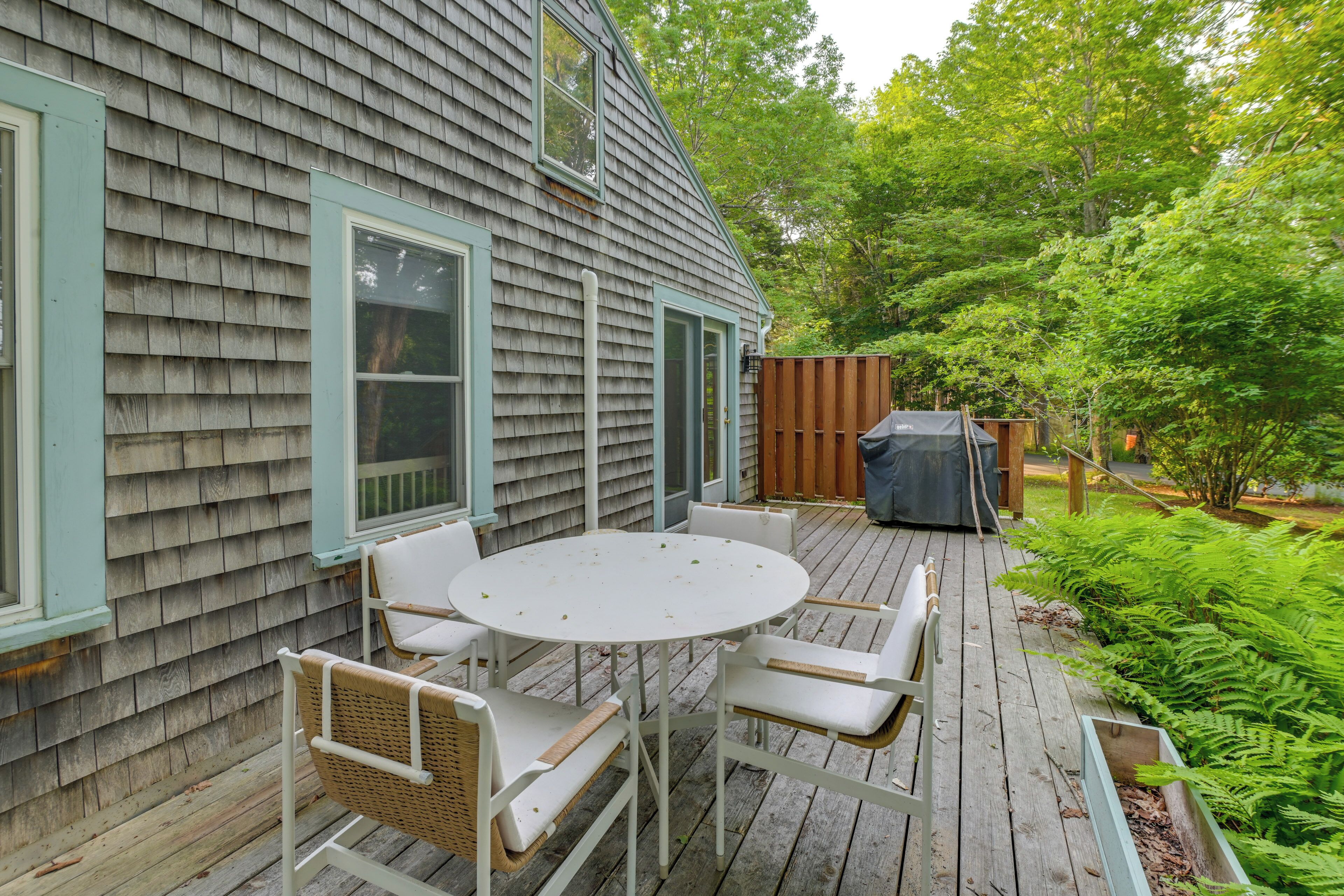 A deck with a round table and four chairs, a grill, and a wooden fence.