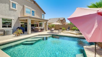 Una piscina con zona de patio, mobiliario exterior y un espacio de estar cubierto.