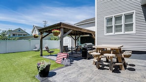 Um quintal com pérgola de madeira, móveis de exterior e espaço para churrasco.