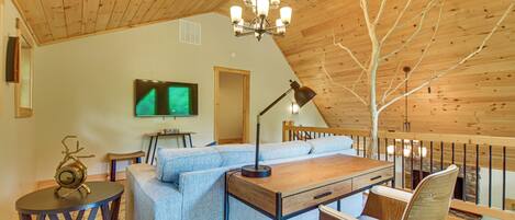 Una habitación acogedora con techo de madera, un sofá, una mesa, un televisor y una silla.